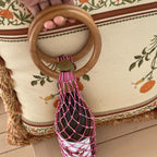 Pink macrame wine bottle carrier with wooden handle, perfect for wine gift accessories and dinner parties.