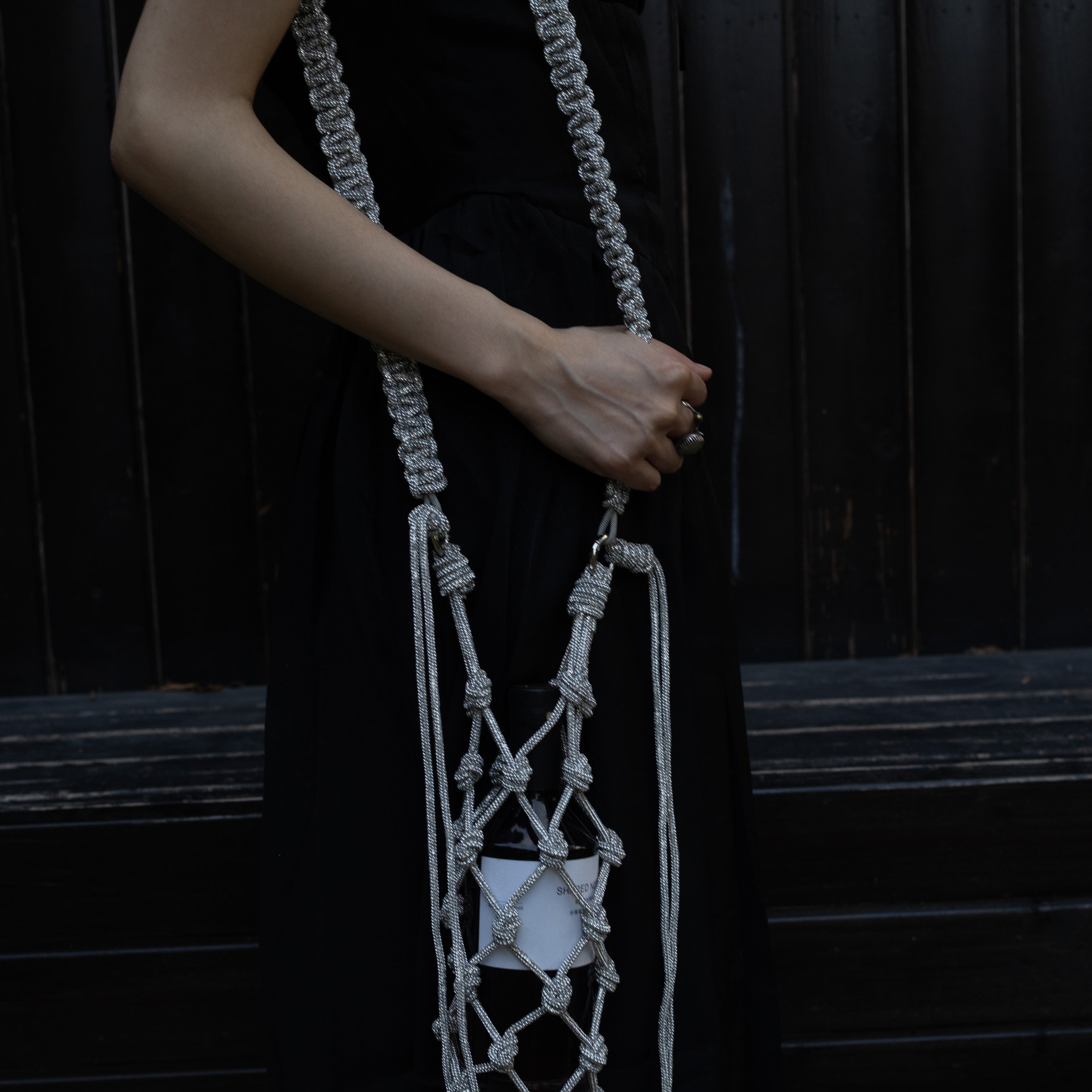 Sparkly silver wine tote bag with knotted design, held by woman in black dress for elegant wine gifting.