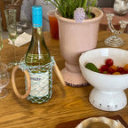 Wine bottle in netted carrier with wooden handle on table, perfect for wine gift accessories and dinner parties
