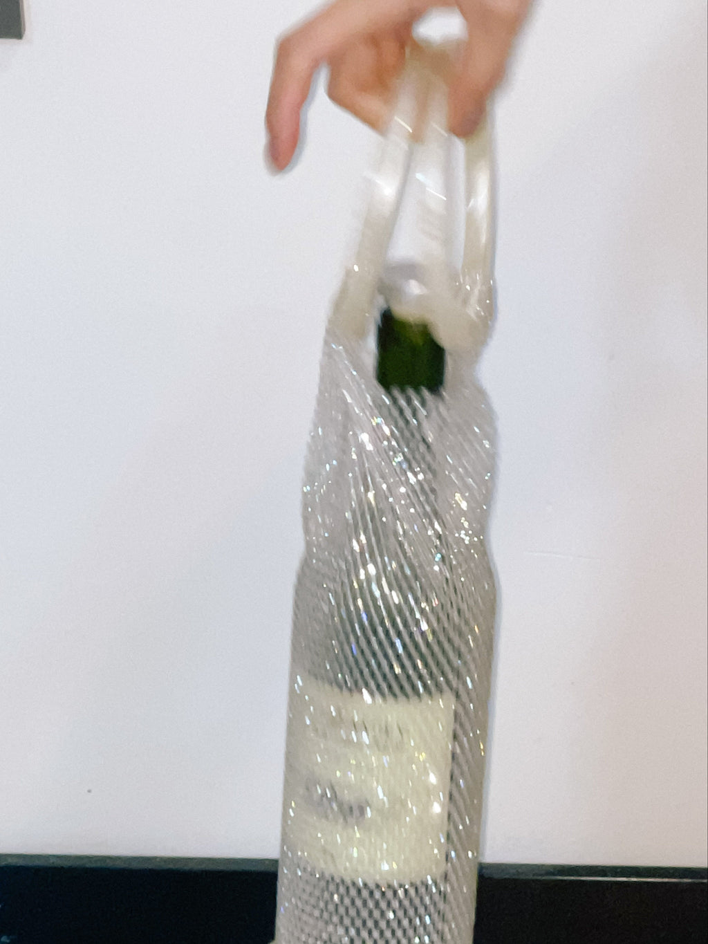Clear crystal wine bag with a green item inside, held by a hand against a white background