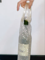 Clear crystal wine bag with a green item inside, held by a hand against a white background